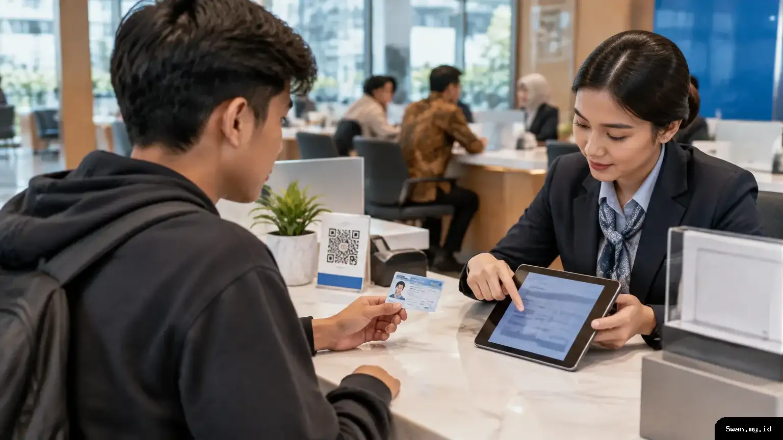 A young Indonesian citizen discusses a new bank account with a staff member at a service counter, representing the proposed NIK-linked account program for 17-year-olds. Young Indonesian citizen discusses a bank account at a service desk
