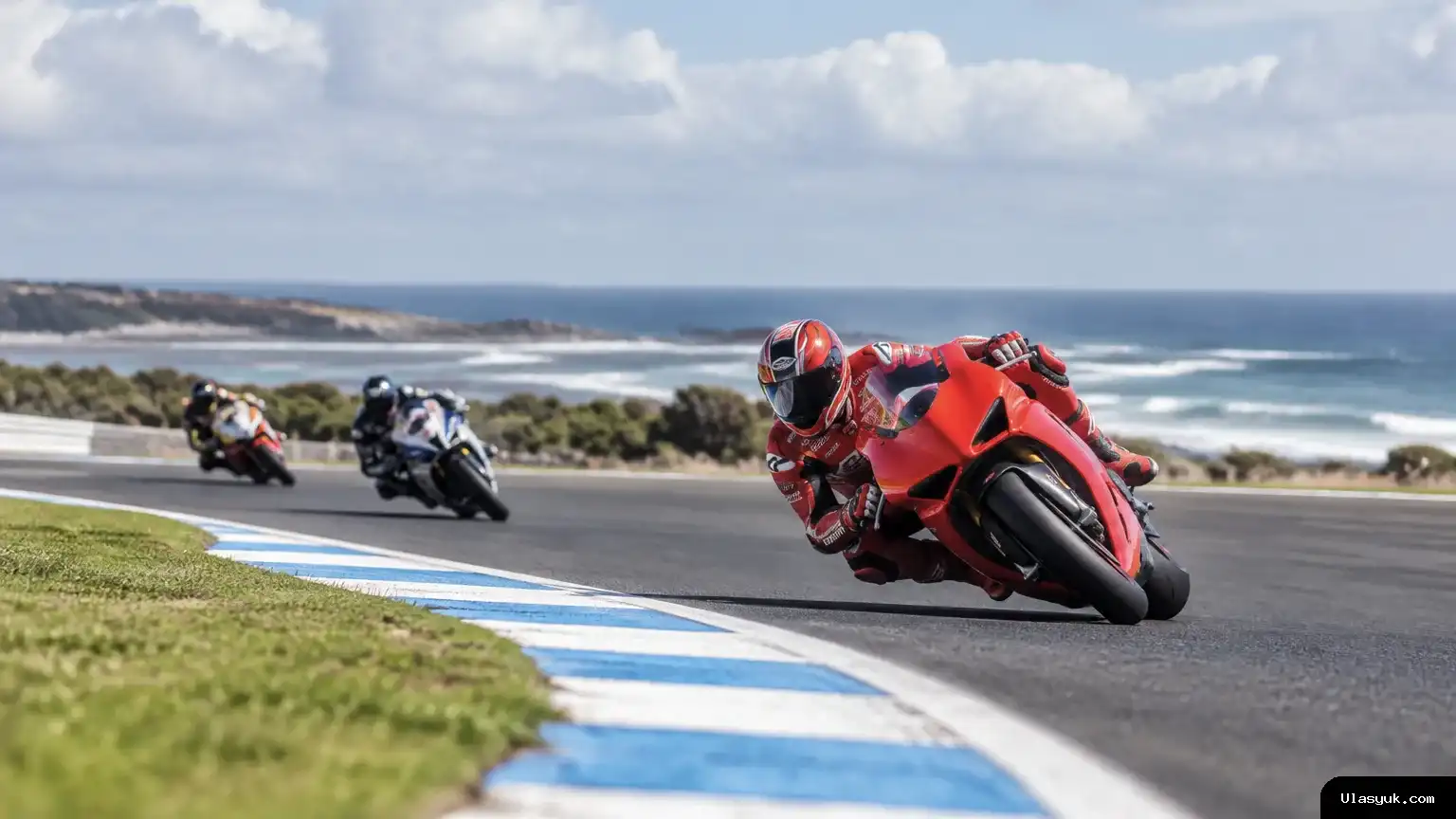 Ilustrasi menampilkan tiga pebalap MotoGP yang sedang melaju di tikungan Sirkuit Phillip Island. Kamera berada dekat permukaan lintasan dan menyorot motor terdepan, sementara dua pebalap lain terlihat di belakang. Tiga motor balap melaju melewati tikungan di Sirkuit Phillip Island.