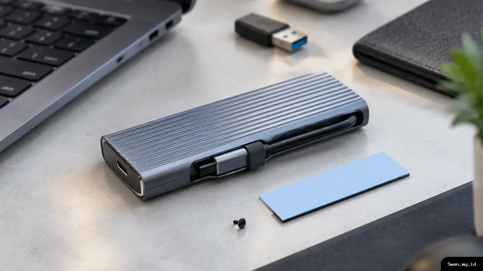 A close editorial view of a compact aluminum SSD enclosure, showing its integrated cable tucked into the side and small installation accessories nearby. Aluminum NVMe SSD enclosure with an attached USB-C cable